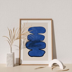 May include: A framed print with a blue abstract design on a beige background. The print is in a wooden frame and is sitting on a white surface.