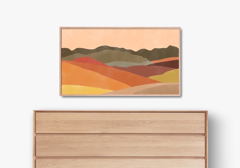 May include: Abstract landscape art print with a colorful mountain range in shades of orange, yellow, brown, and green. The print is framed in a light wood frame.