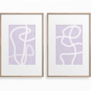 May include: Two framed abstract art prints with a light purple background and white lines. The prints are in simple wooden frames.