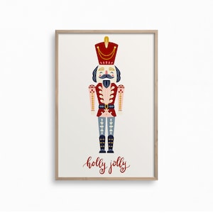 May include: A framed print featuring a colorful illustration of a nutcracker soldier. The nutcracker is depicted in red, blue, and gold, with a large mustache and a tall hat. The words "holly jolly" are written in red script below the nutcracker.