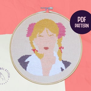 Puede incluir: Patrón de punto de cruz con un retrato de estilo pop art de una mujer con coletas rubias y lazos rosas. El diseño está en un bastidor de bordado de madera. Las palabras "PDF PATTERN" están en un círculo morado.
