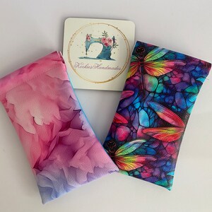May include: Two eyeglass cases with vibrant designs and a coaster. One case has a pink and purple floral pattern, the other a dragonfly design with rainbow colours. The coaster has a sewing machine and the text "Rockies Handmades".