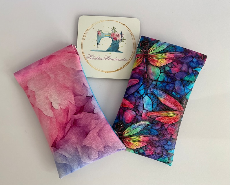 May include: Two eyeglass cases with vibrant designs and a coaster. One case has a pink and purple floral pattern, the other a dragonfly design with rainbow colours. The coaster has a sewing machine and the text "Rockies Handmades".