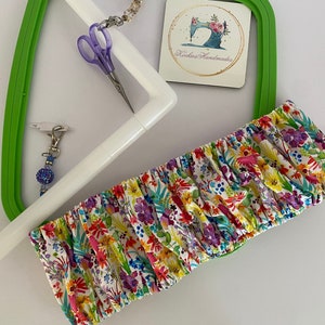 May include: A colourful floral fabric craft accessory with a white and green embroidery hoop, purple scissors, and a beaded charm. The fabric features a pattern of flowers in various colours.