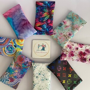 May include: A selection of patterned fabric glasses cases, featuring floral, abstract, and geometric designs. A coaster with a sewing machine logo is in the centre. The cases are arranged on a white surface.