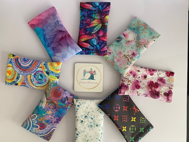 May include: A selection of patterned fabric glasses cases, featuring floral, abstract, and geometric designs. A coaster with a sewing machine logo is in the centre. The cases are arranged on a white surface.