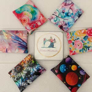 May include: A selection of patterned coin purses displayed around a small card. The purses showcase diverse designs, such as watercolour florals, a sunflower, and a space-themed pattern. The card features a sewing machine logo and the text "Hookies Handmades."
