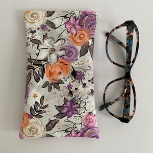 May include: A floral print glasses case with a matching pair of eyeglasses. The case features a pattern of white, orange, and purple flowers with gray leaves on a light gray background. The eyeglasses have a tortoiseshell pattern.