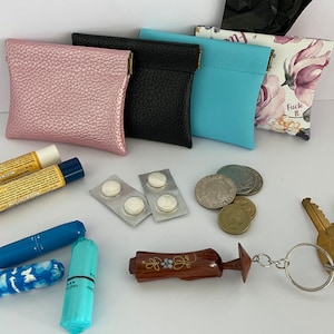 May include: Various small pouches in pink, black, light blue, and floral designs. Also visible are lip balms, pills, coins, keys, and a wooden keychain.