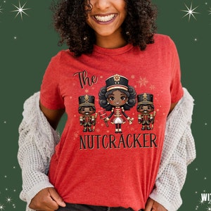 May include: Red t-shirt with a graphic of three cartoon nutcrackers. The center nutcracker is a girl with brown hair and a red and gold uniform. The text "The Nutcracker" is printed below the graphic.