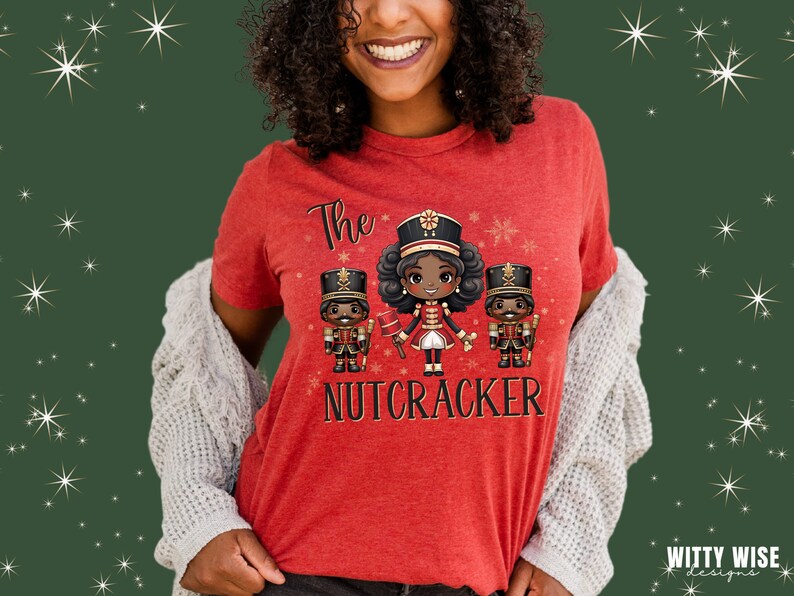 May include: Red t-shirt with a graphic of three cartoon nutcrackers. The center nutcracker is a girl with brown hair and a red and gold uniform. The text "The Nutcracker" is printed below the graphic.