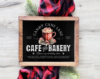 May include: A black chalkboard sign with a white wooden frame, advertising a cafe and bakery called "Candy Cane Lane". The sign features a red and white striped mug with a candy cane handle, filled with marshmallows and topped with whipped cream. The text on the sign reads "Candy Cane Lane Cafe and Bakery, Served Fresh, Served Daily, Have a cup of holiday cheer, Candy Cane Latte, Peppermint Mocha, Maple Pecan Macchiato, Peppermint Bark Cookies, Candy Cane Mocha Crumb Muffins."