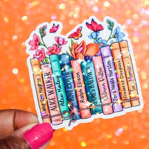 May include: A sticker featuring a stack of books with the names of authors printed on the spines. The books are surrounded by colorful flowers and butterflies. The authors include Langston Hughes, Alice Walker, Alex Haley, Maya Angelou, Ralph Ellison, James Baldwin, Octavia Butler, Zora Neale Hurston, Frederick Douglass, and Toni Morrison.