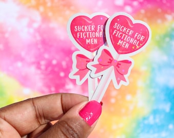 May include: Two pink heart-shaped stickers with a lollipop stick and a pink bow. The stickers say "SUCKER FOR FICTIONAL MEN" with glitter accents.