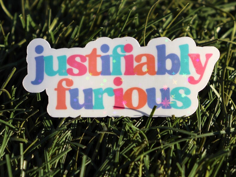 May include: A white sticker with the text "justifiably furious" in rainbow colours with glitter accents.