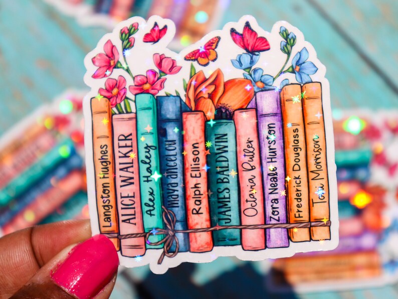 May include: A sticker featuring a stack of books with floral accents and glitter. The books have the names of authors printed on their spines, including Langston Hughes, Alice Walker, Alex Haley, Maya Angelou, Ralph Ellison, James Baldwin, Octavia Butler, Zora Neale Hurston, Frederick Douglass, and Toni Morrison.