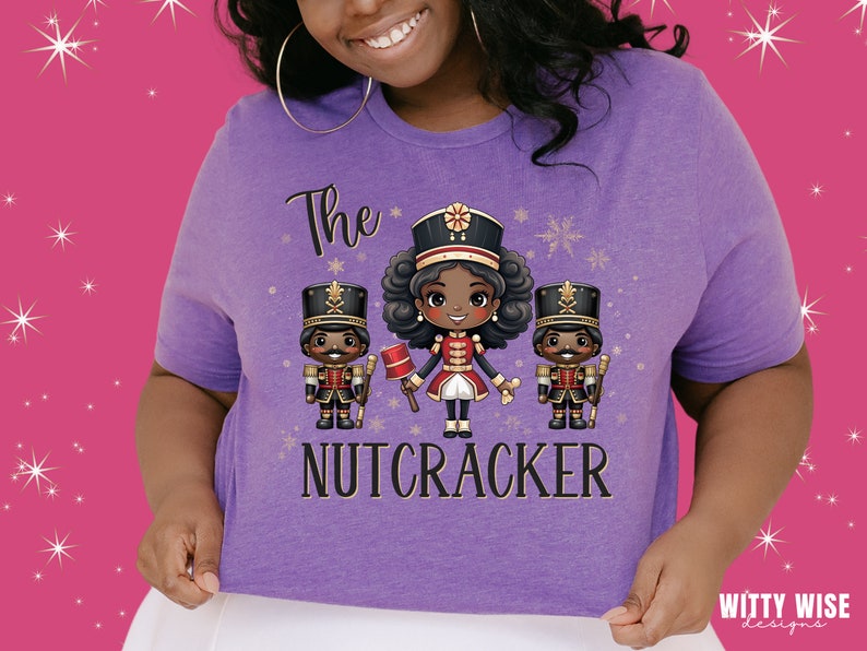 May include: Purple t-shirt with a graphic of three cartoon nutcrackers. The center nutcracker is a girl with brown hair and a red and gold uniform. The text "The Nutcracker" is printed below the graphic.
