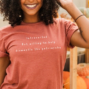 May include: A rust-colored t-shirt with the text "Introverted. But willing to help dismantle the patriarchy." printed in white.