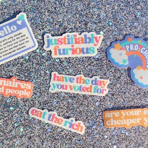 May include: A collection of colourful stickers with various messages, including "hello", "justifiably furious", "billionaires are bad people", "have the day you voted for", "eat the rich", "pro choice", and "are your eggs cheaper yet?"
