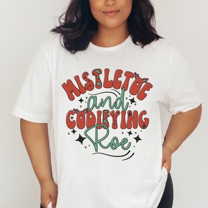 May include: White t-shirt with a red and green graphic that says "Mistletoe and Codfiying Roe".