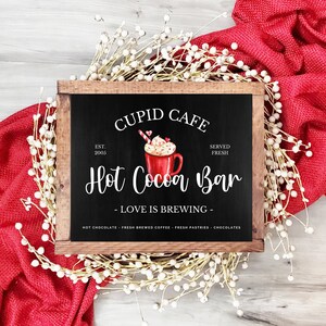 May include: A wooden sign with a chalkboard insert that reads "Cupid Cafe Est. 2005 Served Fresh Hot Cocoa Bar - Love is Brewing - Hot Chocolate Fresh Brewed Coffee Fresh Pastries Chocolates". The sign features a watercolor illustration of a red mug of hot cocoa with whipped cream, candy hearts, and a candy cane.
