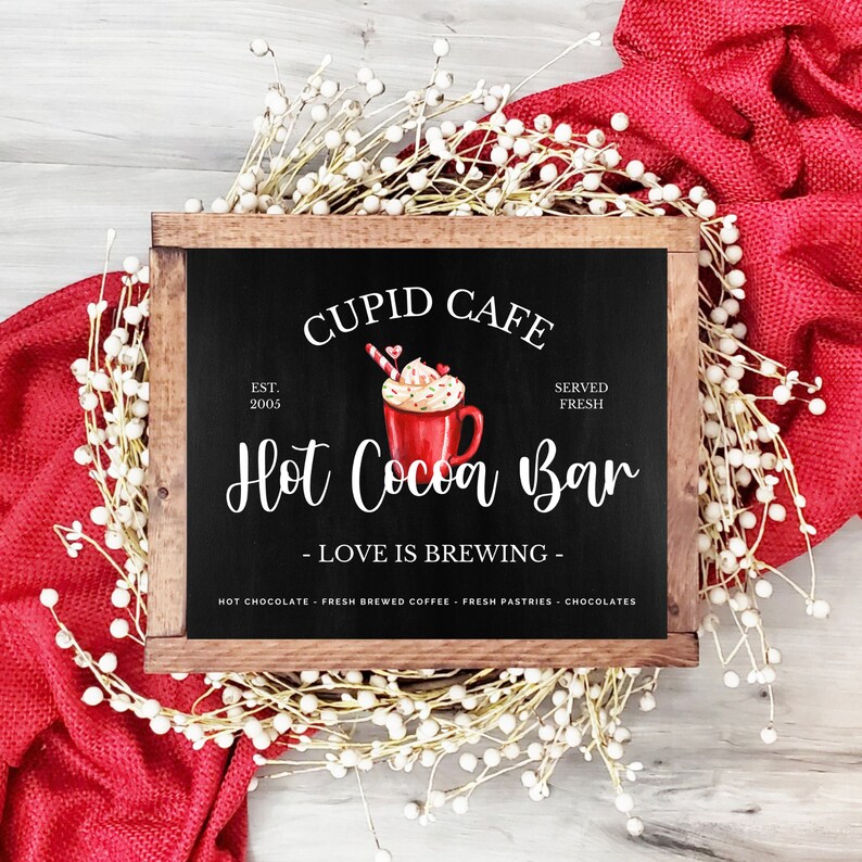 May include: A wooden sign with a chalkboard insert that reads "Cupid Cafe Est. 2005 Served Fresh Hot Cocoa Bar - Love is Brewing - Hot Chocolate Fresh Brewed Coffee Fresh Pastries Chocolates". The sign features a watercolor illustration of a red mug of hot cocoa with whipped cream, candy hearts, and a candy cane.