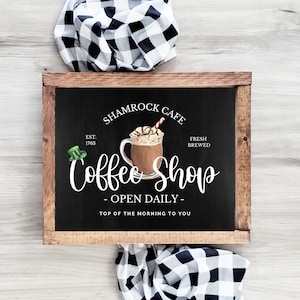 May include: A black chalkboard sign with a wooden frame advertising a coffee shop called "Shamrock Cafe". The sign says "Est. 1763", "Fresh Brewed", "Coffee Shop", "Open Daily", and "Top of the Morning to You". A cartoon image of a coffee drink with whipped cream and a red and white straw is on the sign.