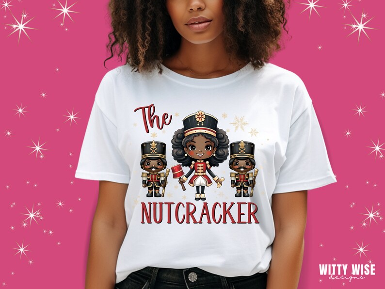 May include: White t-shirt with a graphic of three cartoon nutcrackers. The center nutcracker is a girl with brown skin and curly hair. The text "The Nutcracker" is printed below the graphic.
