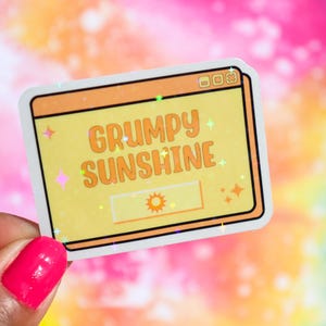 May include: A yellow and orange sticker with a white border. The sticker has a computer window design with the text "GRUMPY SUNSHINE" and a yellow sun icon.