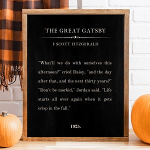 May include: A black chalkboard with a wooden frame displays a quote from "The Great Gatsby" by F. Scott Fitzgerald. The quote reads, "What'll we do with ourselves this afternoon?" cried Daisy, "and the day after that, and the next thirty years?" "Don't be morbid," Jordan said. "Life starts all over again when it gets crisp in the fall." The quote is followed by the year 1925. Two orange pumpkins are in the foreground.