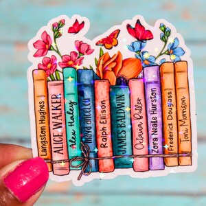 May include: A sticker featuring a stack of books with the names of famous authors, including Langston Hughes, Alice Walker, Alex Haley, Maya Angelou, Ralph Ellison, James Baldwin, Octavia Butler, Zora Neale Hurston, Frederick Douglass, and Toni Morrison. The books are decorated with colorful flowers and butterflies.