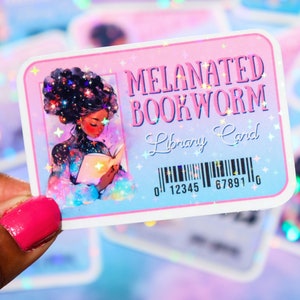 Könnte beinhalten: Ein holografischer Aufkleber in Pink und Blau mit dem Text "MELANATED BOOKWORM Library Card" und einem Barcode. Der Aufkleber zeigt eine Illustration einer schwarzen Frau mit lockigem Haar, die ein Buch liest.