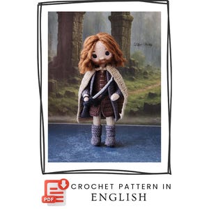 Op de afbeelding: Een handgemaakte gehaakte pop met rood haar, een beige cape en bruine kleding. De pop heeft een baard en houdt een zwaard vast. De achtergrond toont een vage landschap met stenen structuren. De tekst "CROCHET PATTERN IN ENGLISH" is inbegrepen.