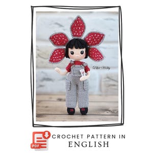 Pode incluir: Boneca de crochê feita à mão com um adorno de cabeça de flor Demogorgon. A boneca usa uma camisa vermelha, macacão cinza e sapatos pretos. O texto "CROCHET PATTERN IN ENGLISH" é exibido abaixo.