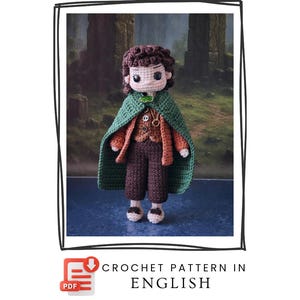 Puede incluir: Muñeco de ganchillo hecho a mano de un personaje de novela fantástica, con capa verde, pantalón marrón y camisa naranja. El muñeco tiene pelo castaño y un broche verde en forma de hoja. Incluye el texto "CROCHET PATTERN IN ENGLISH".