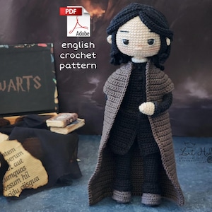 May include: Crocheted amigurumi doll of a young person with black hair wearing a brown cloak and black clothing. The doll is standing on a blue surface. The text "HOGWARTS" is visible in the background.