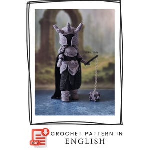 Könnte beinhalten: Eine gehäkelte Ritterpuppe in Grau- und Schwarztönen, komplett mit Helm, Rüstung und Umhang. Die Puppe hält eine Flegel. Das Bild enthält den Text "CROCHET PATTERN IN ENGLISH".