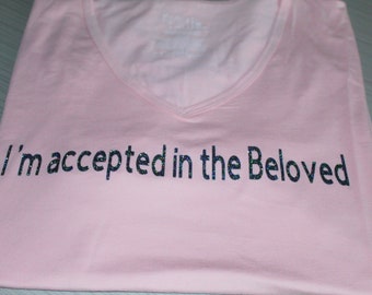May include: Pink t-shirt with the text "I'm accepted in the Beloved" printed in black glitter.
