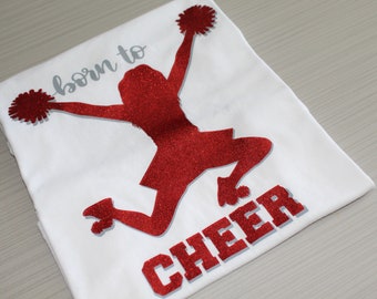 Girls short-sleeved cotton t-shirt with Born to Cheer'' letters and silhouette of a cheerleader in glitter.