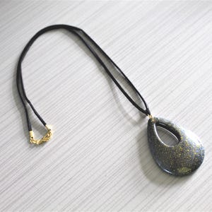Black with gold glitter teardrop-shaped pendant with cutout design, on a 32 1/2 inch black suede cord with lobster clasp closure.