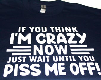 May include: Navy blue t-shirt with a bold white graphic. The text reads: "IF YOU THINK I'M CRAZY NOW JUST WAIT UNTIL YOU PISS ME OFF!" The shirt has a crew neck and a tag at the neckline.