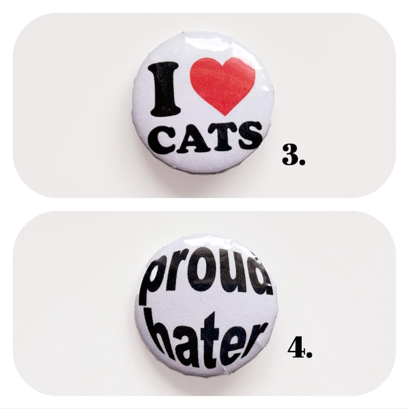 以下が含まれることがあります： 2つの丸い白いボタン。1つのボタンには赤いハートマークと「I ❤️ CATS」の文字が書かれています。もう1つのボタンには黒い文字で「proud hater」と書かれています。どちらのボタンも白い背景にあります。
