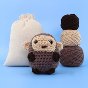 May include: A brown crocheted monkey toy with a beige face and brown balls of yarn in the background.