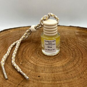 May include: A yellow glass car diffuser with a white cap and a gold string. The diffuser has the text "Candles & Lights Make Everything Nice Diva Car diffuser 8ml" printed on the label.