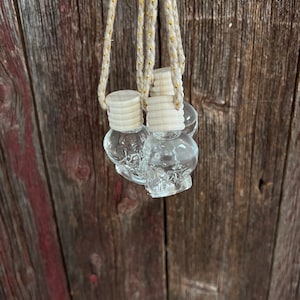 May include: Three clear glass skull-shaped car air fresheners hanging from a white string with gold accents. The fresheners are attached to the string with white wooden beads.