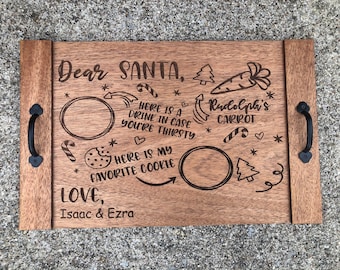 May include: A wooden tray with a Christmas theme. It has a message that says "Dear Santa" and includes spaces for a drink and a cookie. The tray also has a drawing of a carrot with the text "Rudolph's Carrot". The tray is signed "Love, Isaac & Ezra".