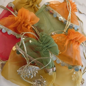 May include: Assortment of small, colorful, sheer drawstring bags with gold trim and sequins. The bags are made of a delicate, translucent fabric and have a gathered, ruffled appearance.