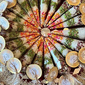 May include: A tray of small, clear cones filled with colorful candies and spices. Each cone has a small, round tag attached with the text "Anja Mehndi 11/09/2023" printed on it.
