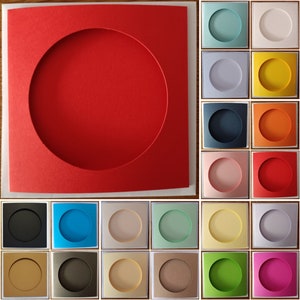 Puede incluir: Una colección de tarjetas cuadradas que presentan una gran ventana circular troquelada en el centro. Las tarjetas están disponibles en una amplia variedad de colores sólidos, incluyendo rojo, azul, amarillo, naranja, verde, rosa, negro, blanco y varios tonos neutros.