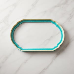 Könnte beinhalten: Ein ovales Tablett mit gewelltem Randdesign. Das Tablett verfügt über eine leuchtend türkisfarbene Innenfläche und einen hellbeigen oder cremefarbenen Außenrand, was einen deutlichen Kontrast zwischen dem Innenbecken und dem erhöhten Rand erzeugt.